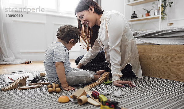 Glückliche Mutter und kleiner Junge spielen zu Hause mit Spielzeug auf dem Teppich