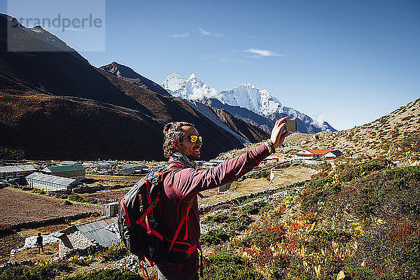 Männlicher Wanderer  der im Sagarmatha-Nationalpark auf einem Berg vor blauem Himmel steht und sich dabei Selbsthilfe nimmt
