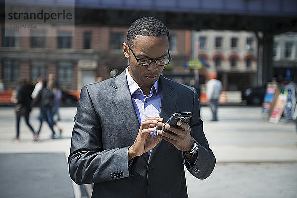 Frontansicht eines Geschäftsmannes  der ein Smartphone auf der Straße benutzt