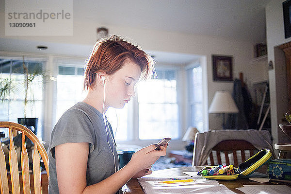 Seitenansicht einer Teenagerin  die ein Mobiltelefon benutzt  während sie zu Hause auf einem Stuhl sitzt