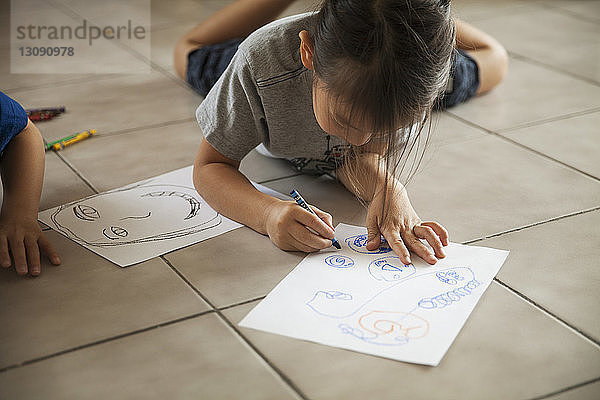 Mädchen  das auf Papier zeichnet  während es neben seinem Bruder zu Hause auf dem Boden liegt