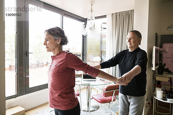 Älterer Mann unterstützt Frau bei der Yoga-Praxis zu Hause