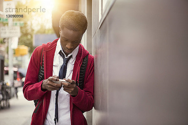 Student telefoniert  während er sich in der Stadt an eine Wand lehnt