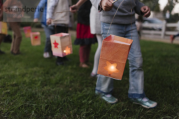 Niedriger Teil von Kindern  die beim Gehen auf dem Feld beleuchtete Papierlaternen tragen
