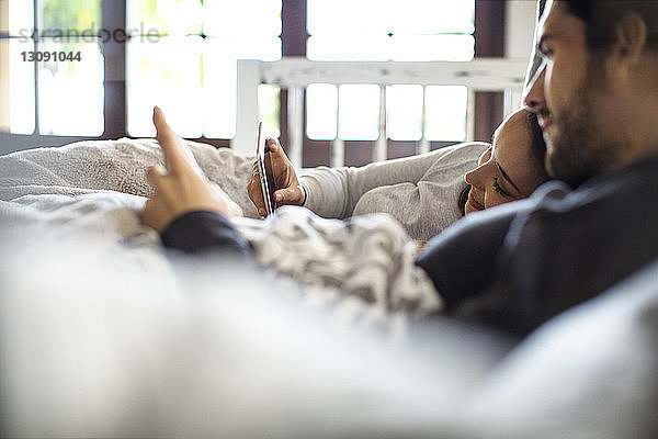 Seitenansicht eines Paares  das Smartphones benutzt  während es zu Hause im Bett liegt