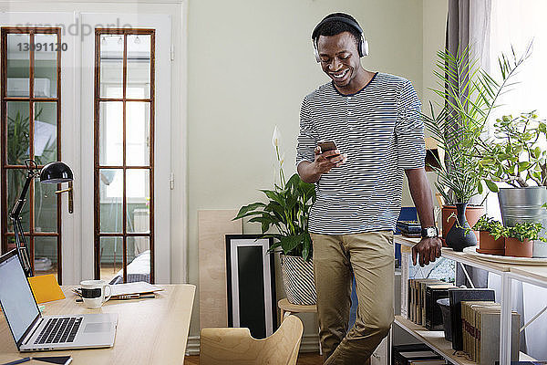 Glücklicher Mann benutzt Smartphone im Heimbüro