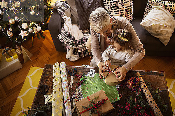 Draufsicht eines Mädchens und einer Großmutter  die zu Weihnachten ein Geschenk bei Tisch einpacken