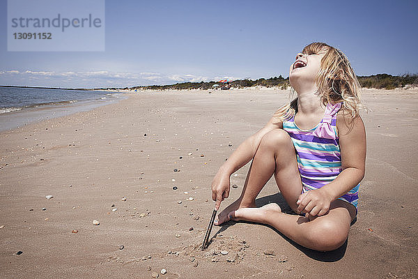 Glückliches Mädchen mit dem Kopf nach hinten auf Sand am Strand sitzend