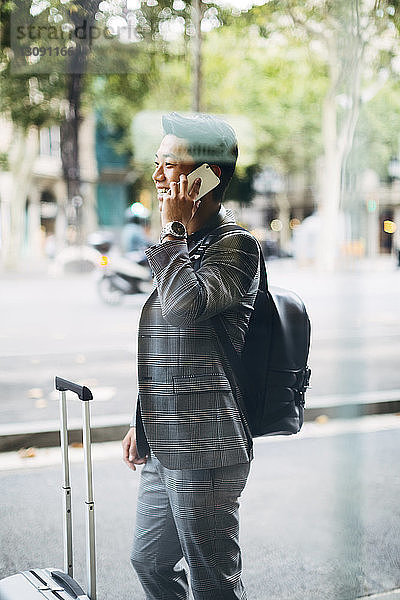 Geschäftsmann mit Gepäck  der am Smartphone telefoniert  durch Fenster gesehen