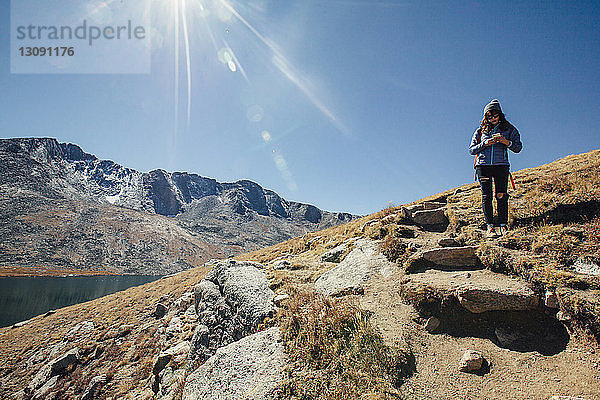 Wanderin benutzt Mobiltelefon  während sie am Berg vor blauem Himmel steht