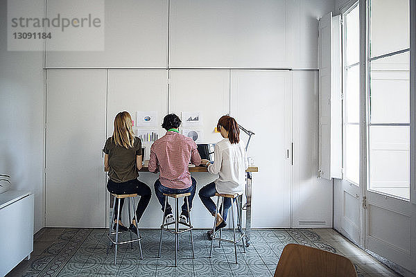 Rückansicht von Geschäftsleuten  die auf Hockern sitzen  während sie im Kreativbüro arbeiten