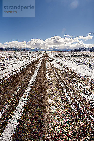 Unbefestigte Straße inmitten einer verschneiten Wüste gegen den Himmel im Winter