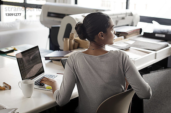 Rückansicht eines Innenarchitekten  der bei der Arbeit am Schreibtisch im Büro wegschaut