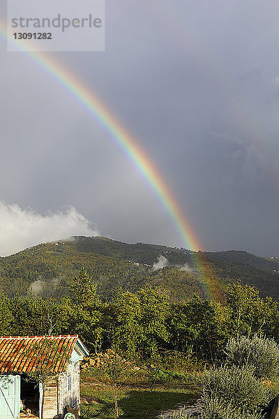 Landschaftliche Ansicht des Regenbogens über den Bergen vor bewölktem Himmel