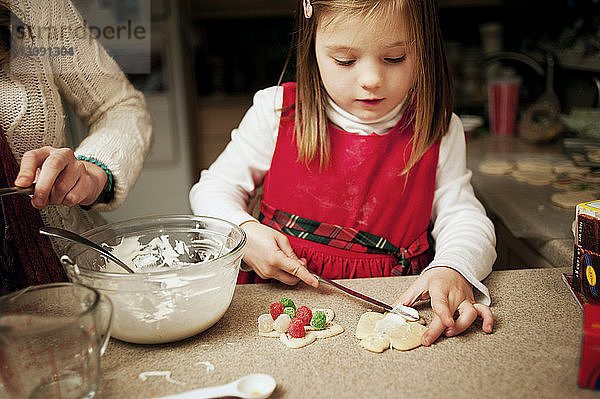 Schwester hilft Mädchen beim Dekorieren von Keksen an der Küchentheke