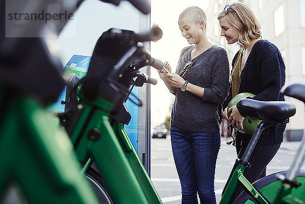 Frau benutzt Mobiltelefon  während sie mit einem Freund am Fahrradparkplatz steht