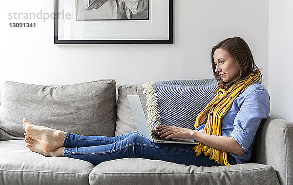 Seitenansicht einer Frau  die einen Laptop-Computer benutzt  während sie auf dem Sofa im Wohnzimmer sitzt