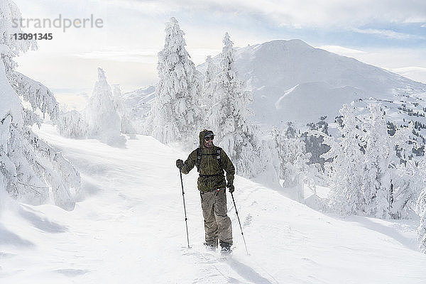 Mann in voller Länge mit Skiausrüstung steht bei nebligem Wetter auf schneebedecktem Berg