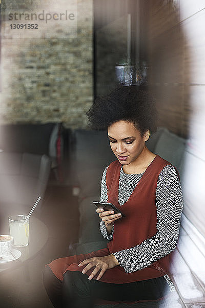 Geschäftsfrau benutzt Smartphone  während sie im Café auf dem Sofa sitzt