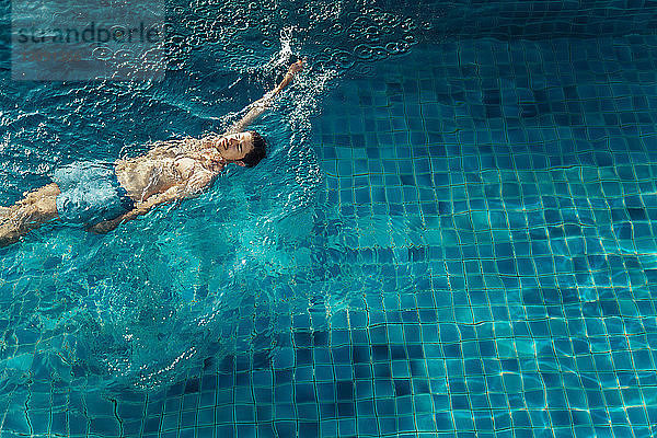 Hochwinkelansicht eines Mannes  der im Schwimmbad eines Touristenortes schwimmt