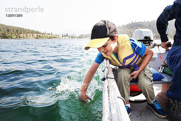 Glücklicher Sohn spielt im Wasser  während er mit seinem Vater im Motorboot auf dem See unterwegs ist