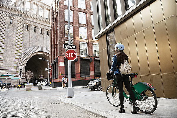Frau geht mit dem Fahrrad auf dem Bürgersteig an einem Gebäude in der Stadt vorbei