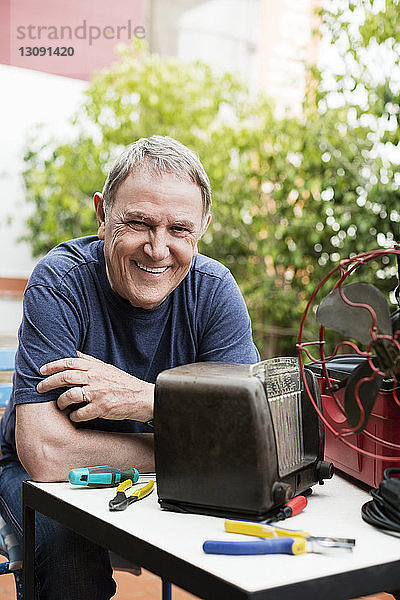 Porträt eines glücklichen älteren Mannes  der ein altes Radio im Hof repariert