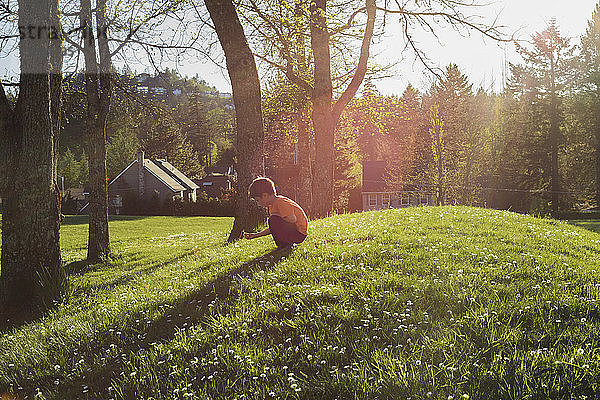 Seitenansicht eines Jungen  der an einem sonnigen Tag auf einem Grasfeld kauert