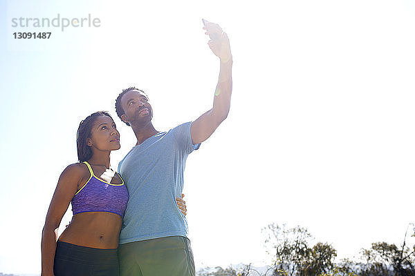 Niedrigwinkelansicht eines Paares  das sich bei klarem Himmel durch ein Mobiltelefon selbstständig macht