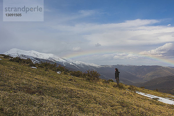 Wanderer steht im Winter gegen Berge und Regenbogen