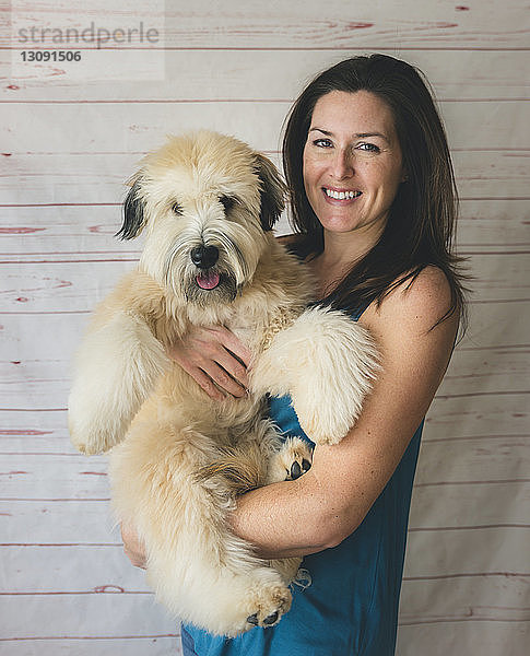 Porträt einer glücklichen Frau  die einen Hund trägt  während sie vor einem Vorhang steht