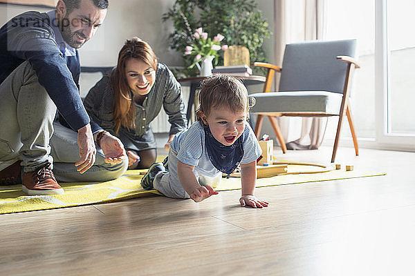 Glückliche Eltern sehen ihren Sohn zu Hause auf dem Boden krabbeln