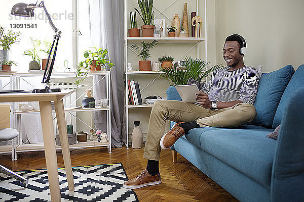 Glücklicher Mann benutzt Tablet-Computer  während er zu Hause auf dem Sofa sitzt