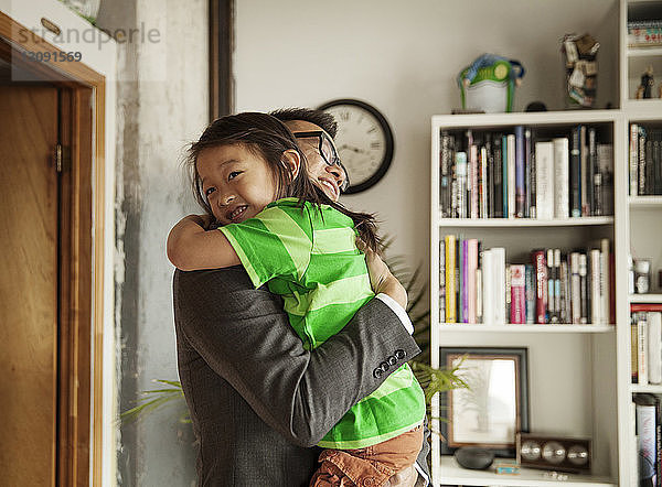 Glücklicher Vater umarmt Tochter  während er zu Hause im Wohnzimmer steht