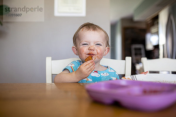 Porträt eines kleinen Mädchens  das zu Hause am Tisch sitzt und Nahrung zu sich nimmt