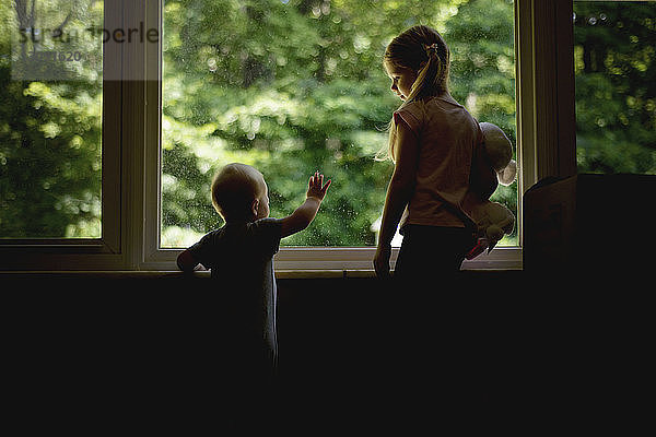 Mädchen schaut den Bruder an  während sie am Fenster steht