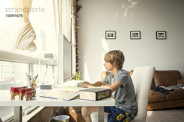 Seitenansicht eines Jungen  der einen Desktop-Computer benutzt  während er am Tisch sitzt