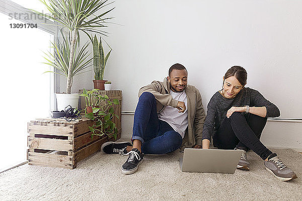 Lächelnde Geschäftsleute  die einen Laptop benutzen  während sie im Kreativbüro am Boden sitzen