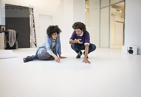 Junge Geschäftskollegen diskutieren über Diagramme  während sie im Kreativbüro am Boden sitzen