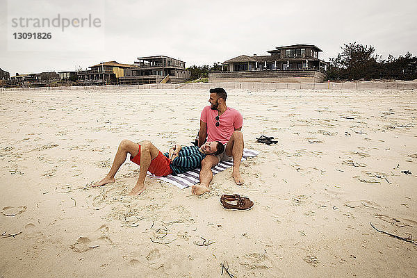 Glückliches homosexuelles Paar ruht sich am Strand gegen den Himmel