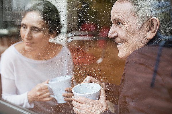 Glückliches älteres Ehepaar schaut zu Hause durchs Fenster