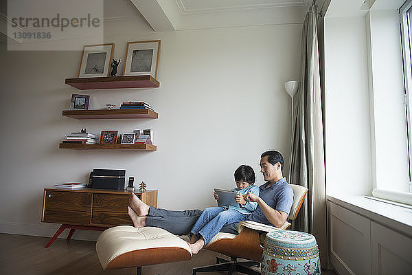 Vater und Sohn benutzen Tabletten  während sie zu Hause an der Wand sitzen