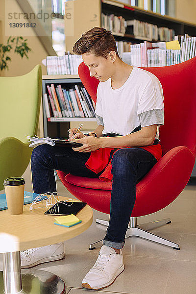 Mann schreibt  während er auf einem Stuhl in der Bibliothek sitzt