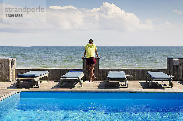 Rückansicht eines am Pool stehenden schwulen Mannes  der das Meer gegen den Himmel betrachtet