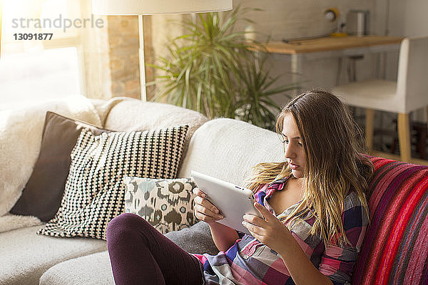 Hochwinkelansicht eines Mädchens  das einen Tablet-Computer benutzt  während es zu Hause auf dem Sofa sitzt