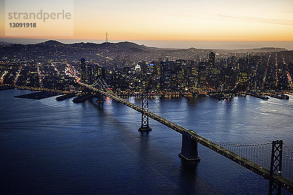 Luftaufnahme der Bay Bridge und der beleuchteten Stadtlandschaft bei Sonnenuntergang
