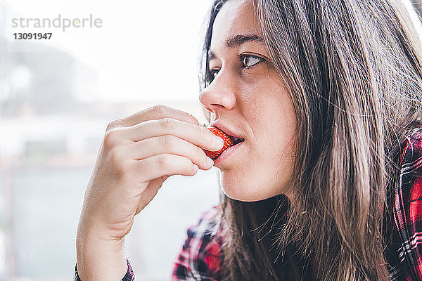 Nahaufnahme einer nachdenklichen Frau  die in einem Café am Fenster Erdbeeren isst