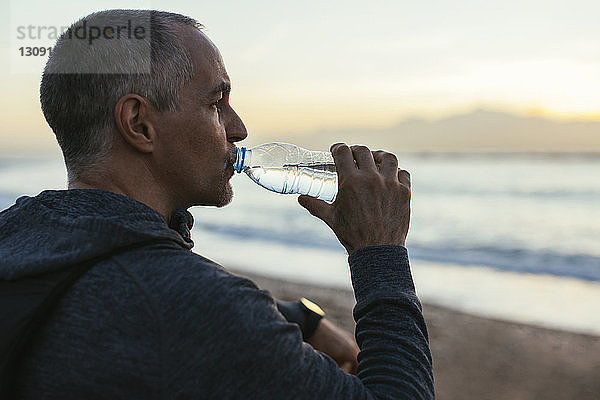Seitenansicht eines Mannes  der Wasser am Strand trinkt