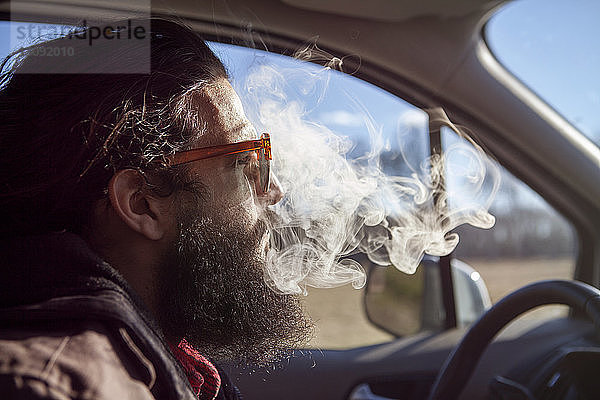 Seitenansicht eines Hipsters  der während des Urlaubs im Auto raucht