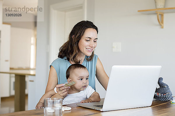 Frau mit kleinem Jungen kauft online ein  während sie zu Hause einen Laptop benutzt